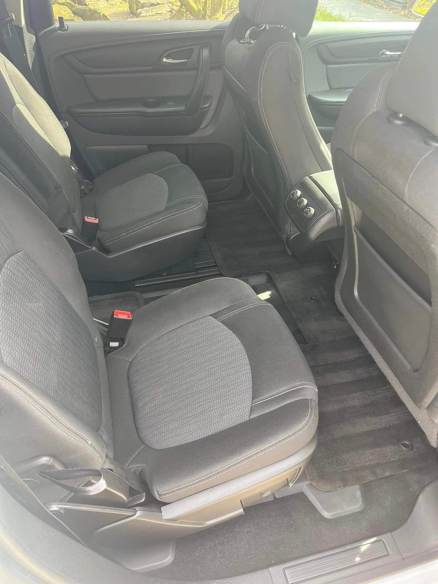 The interior of a car’s back seat featuring black textured upholstery and a child booster seat.