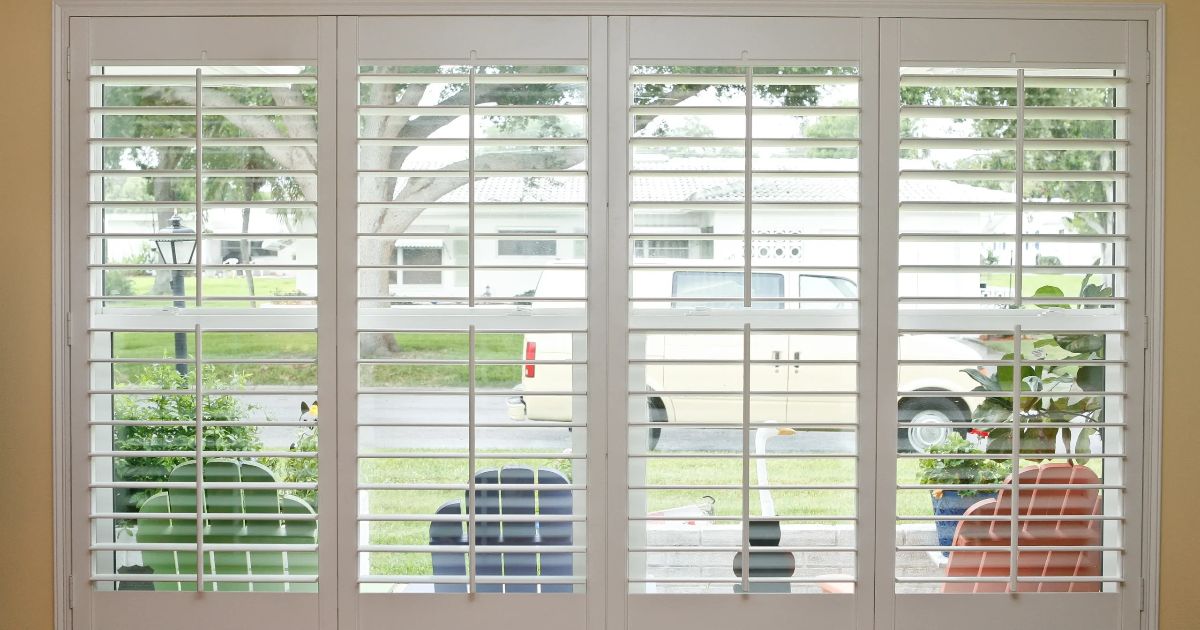 A window with shutters on it looking out to a yard