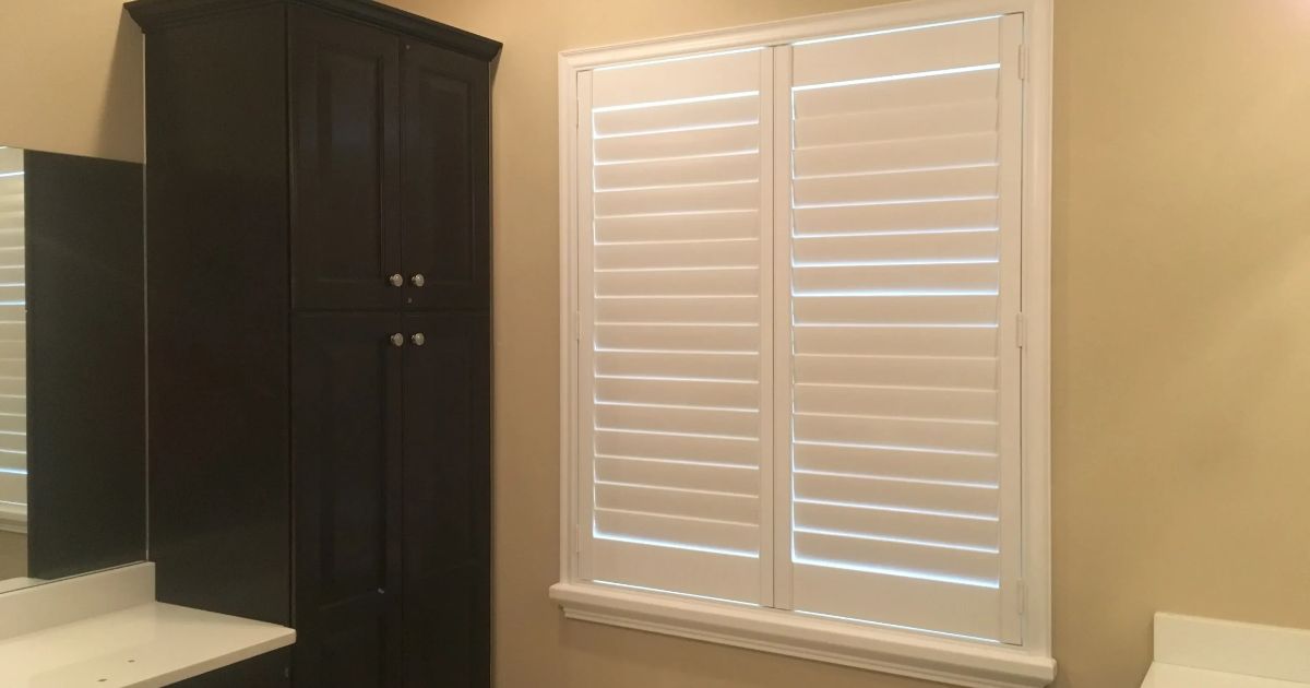 A bathroom with a window and shutters on it.