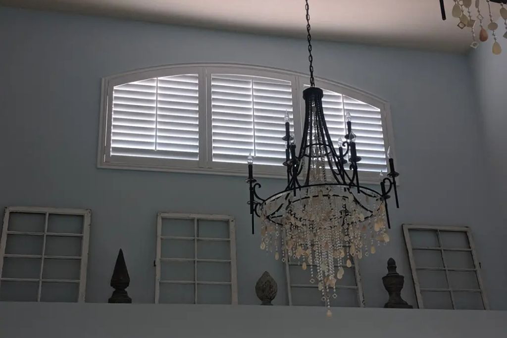 A chandelier is hanging from the ceiling in front of a window with shutters
