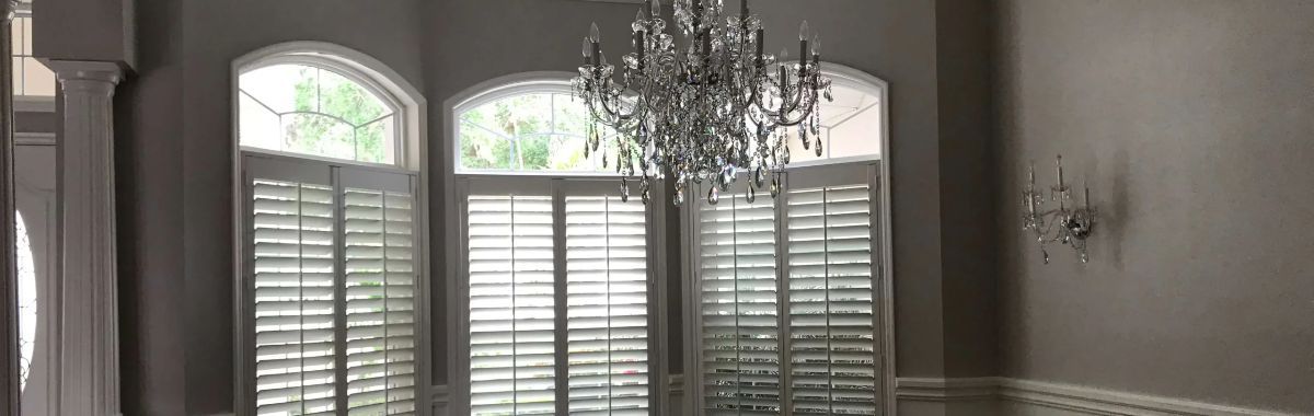 An empty dining room with shutters and a chandelier.