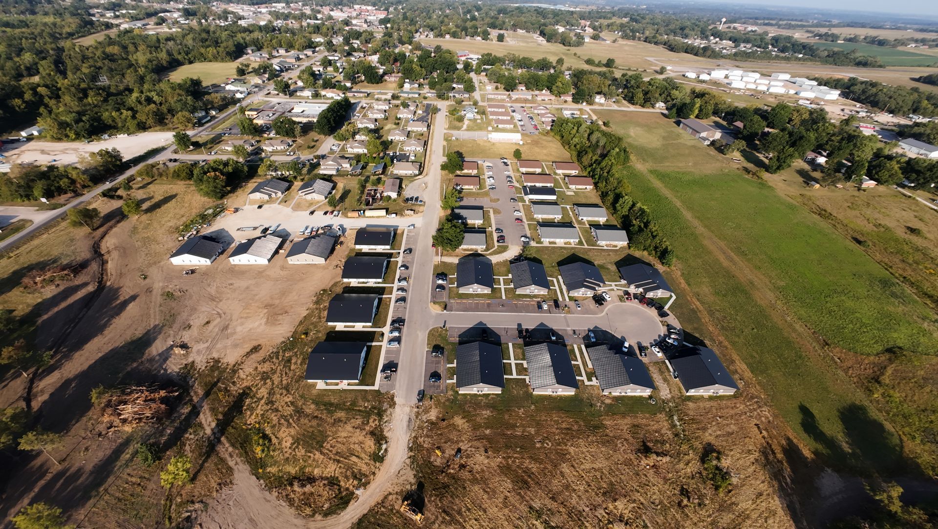 Aerial view of a residential neighborhood with rows of houses, trees, and fields in a rural setting.