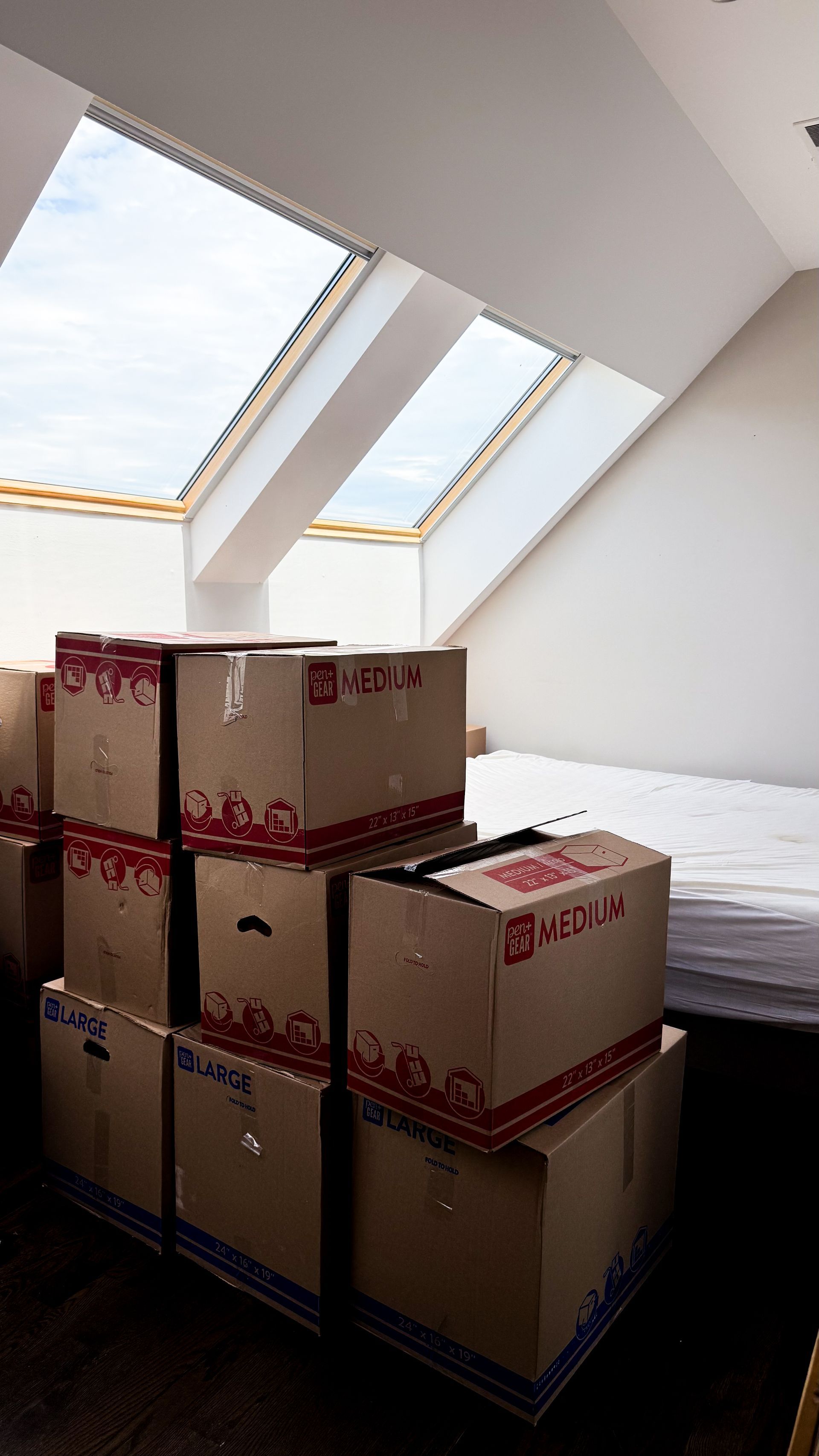 Cardboard boxes stacked in a room with a skylight, indicating moving or storage.