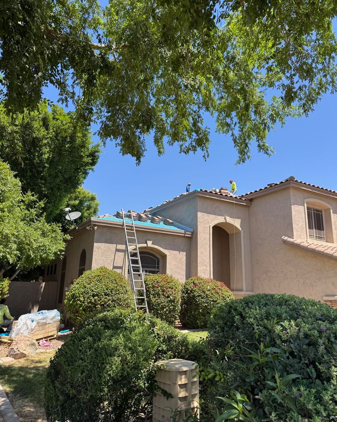 Construction workers on the roof of a stucco house with an extension ladder resting against the eave.