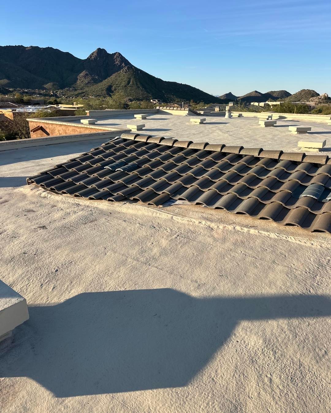 A flat, light-colored roof with a rectangular section of dark, sloped clay tiles, set against a mountainous desert backdrop.