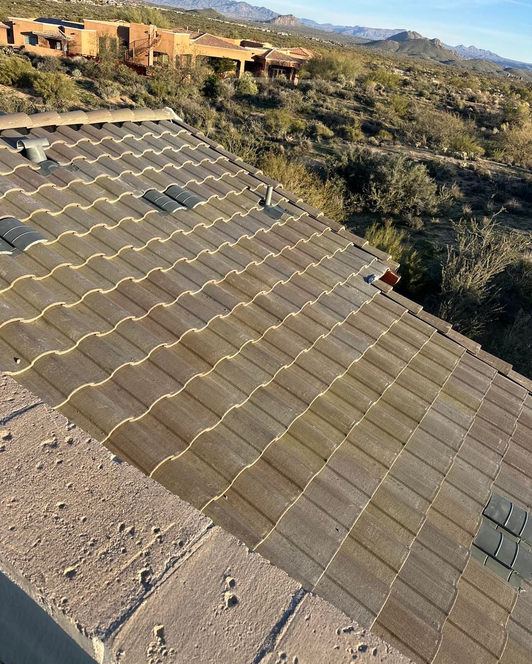 A high-angle view of a brown, tiled roof sloping downward, overlooking a desert landscape with mountains in the distance.