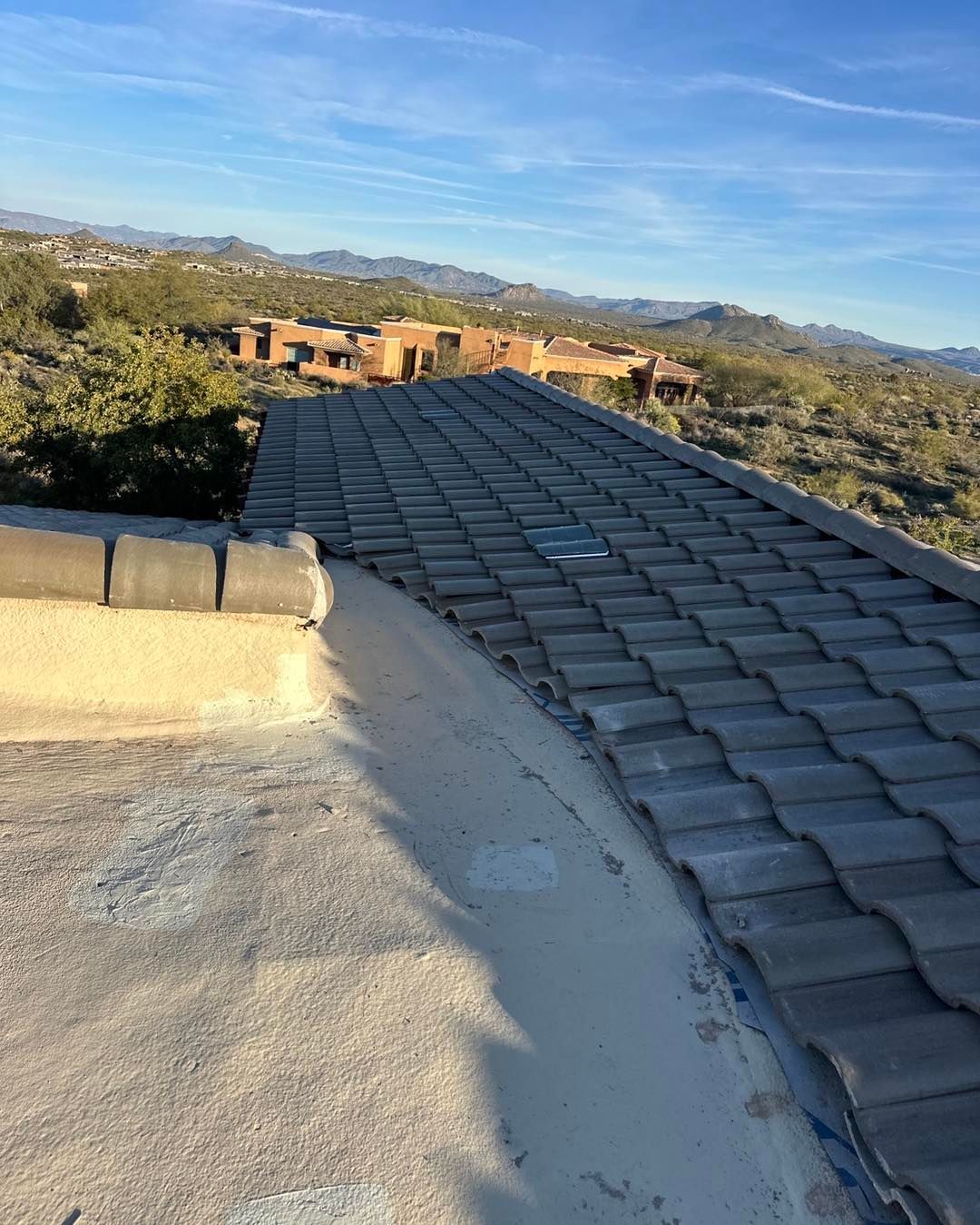 A high-angle view of a tiled roof section meeting a flat, light-colored roof surface against a desert mountain backdrop.