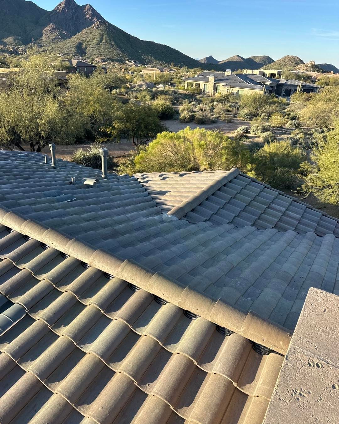 A high-angle view of a grey tiled roof overlooking a desert landscape with scrub vegetation and distant mountains.