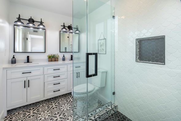 Modern bathroom with white cabinets, double vanity, patterned tile floor, and a glass-enclosed shower with a wall niche.