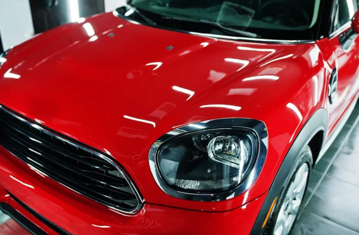 Vast lake shimmers under a bright sun, surrounded by mountains and trees. Rocky foreground. Blue sky.