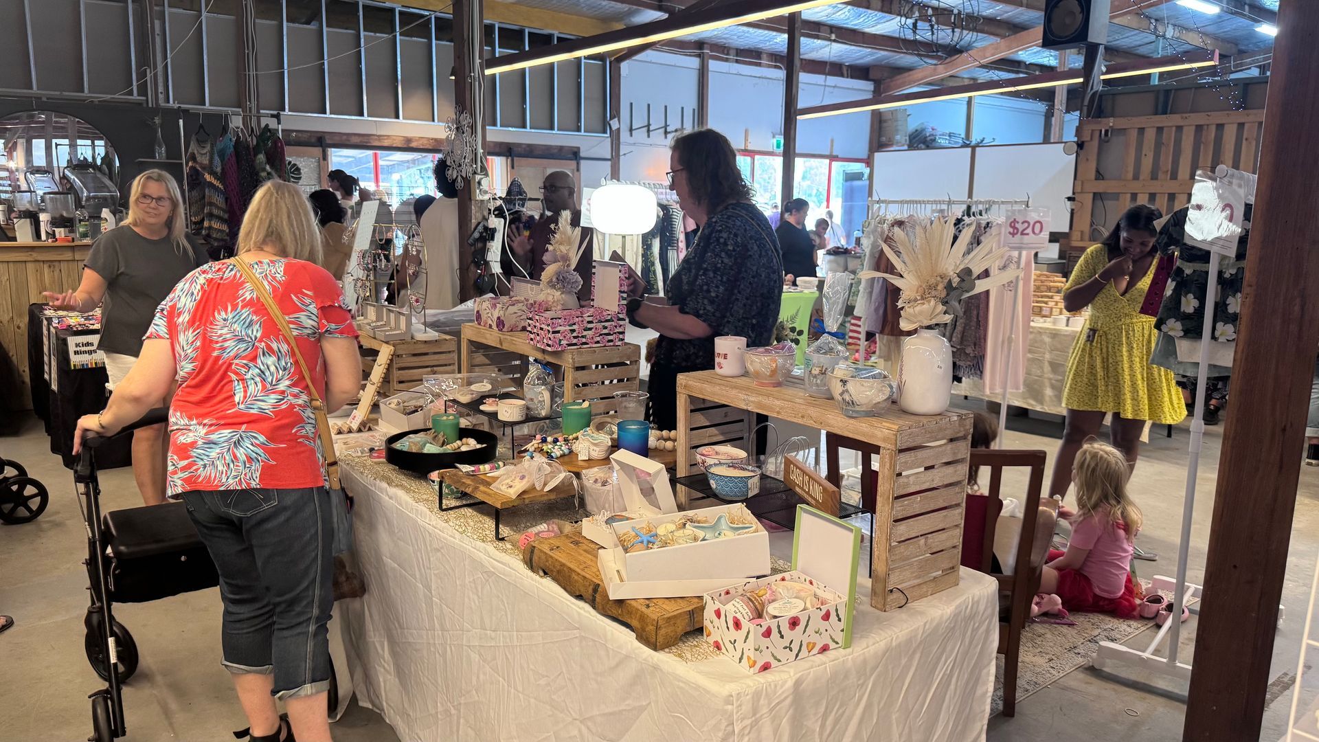 People browsing crafts at a market stall with baked goods and floral decorations, indoors — Rustique on the Coast In Ourimbah, NSW