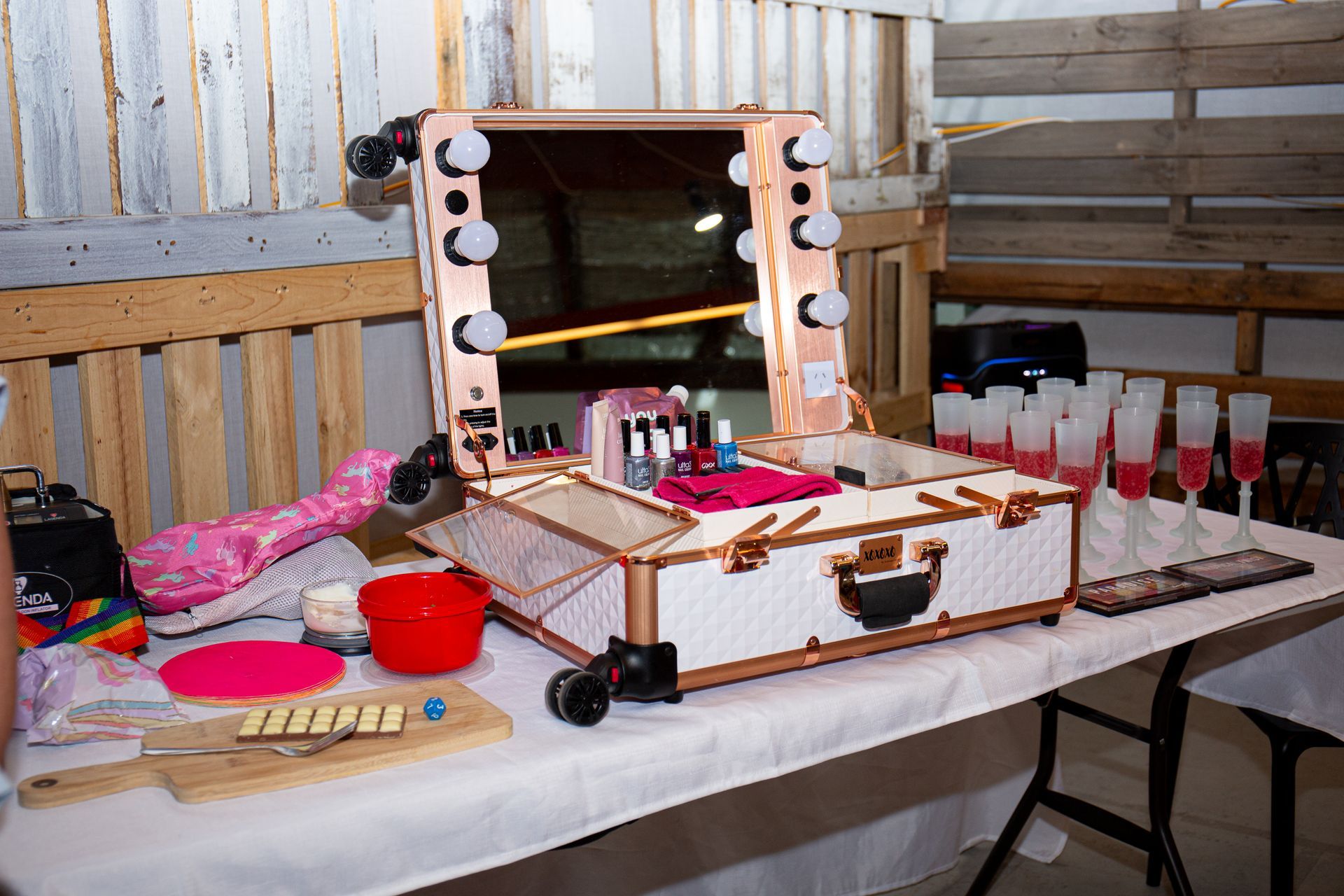 Makeup station with illuminated mirror on a table, plus drinks and accessories.