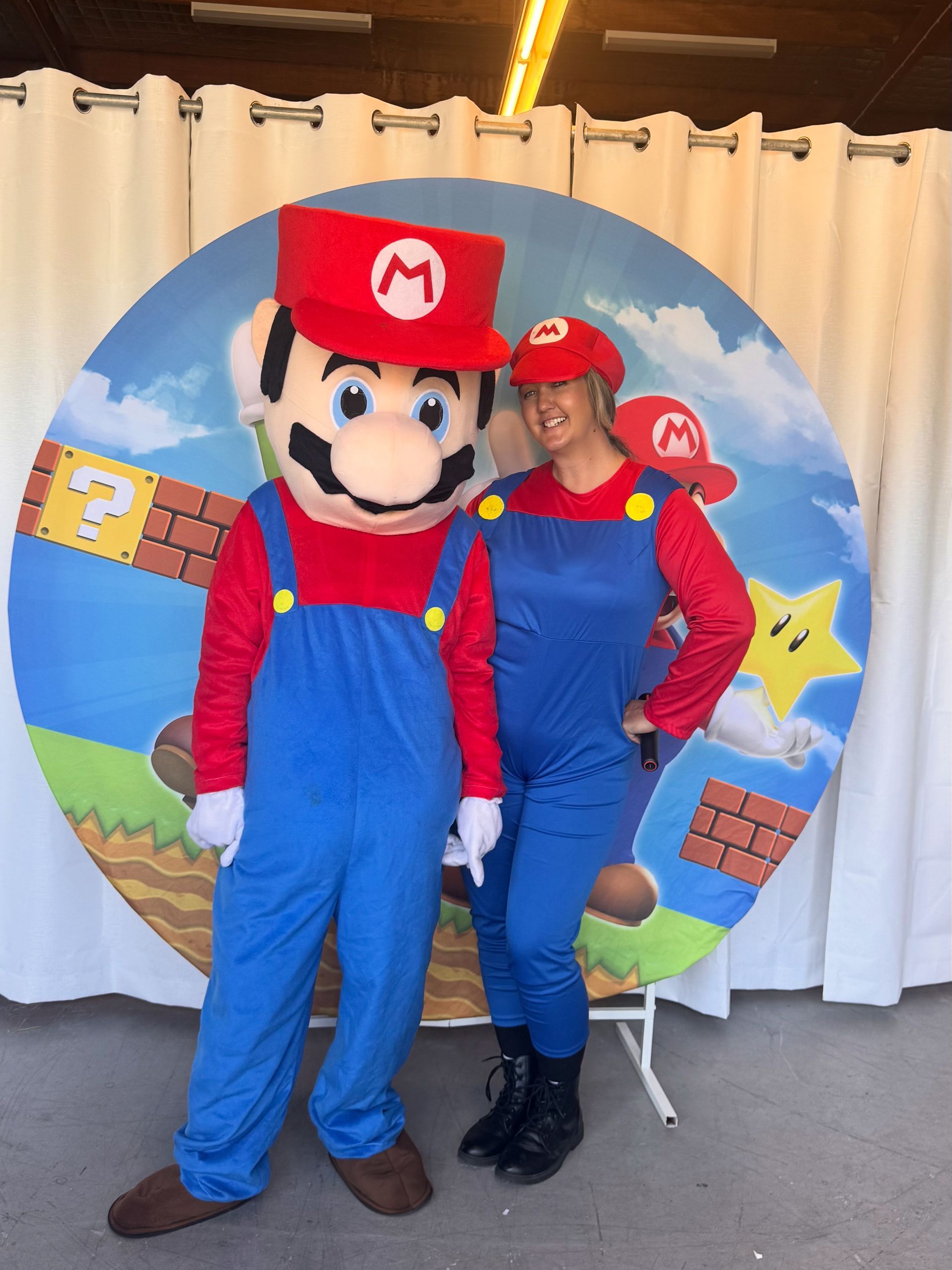 Mario and woman in Mario costumes pose in front of a themed backdrop.