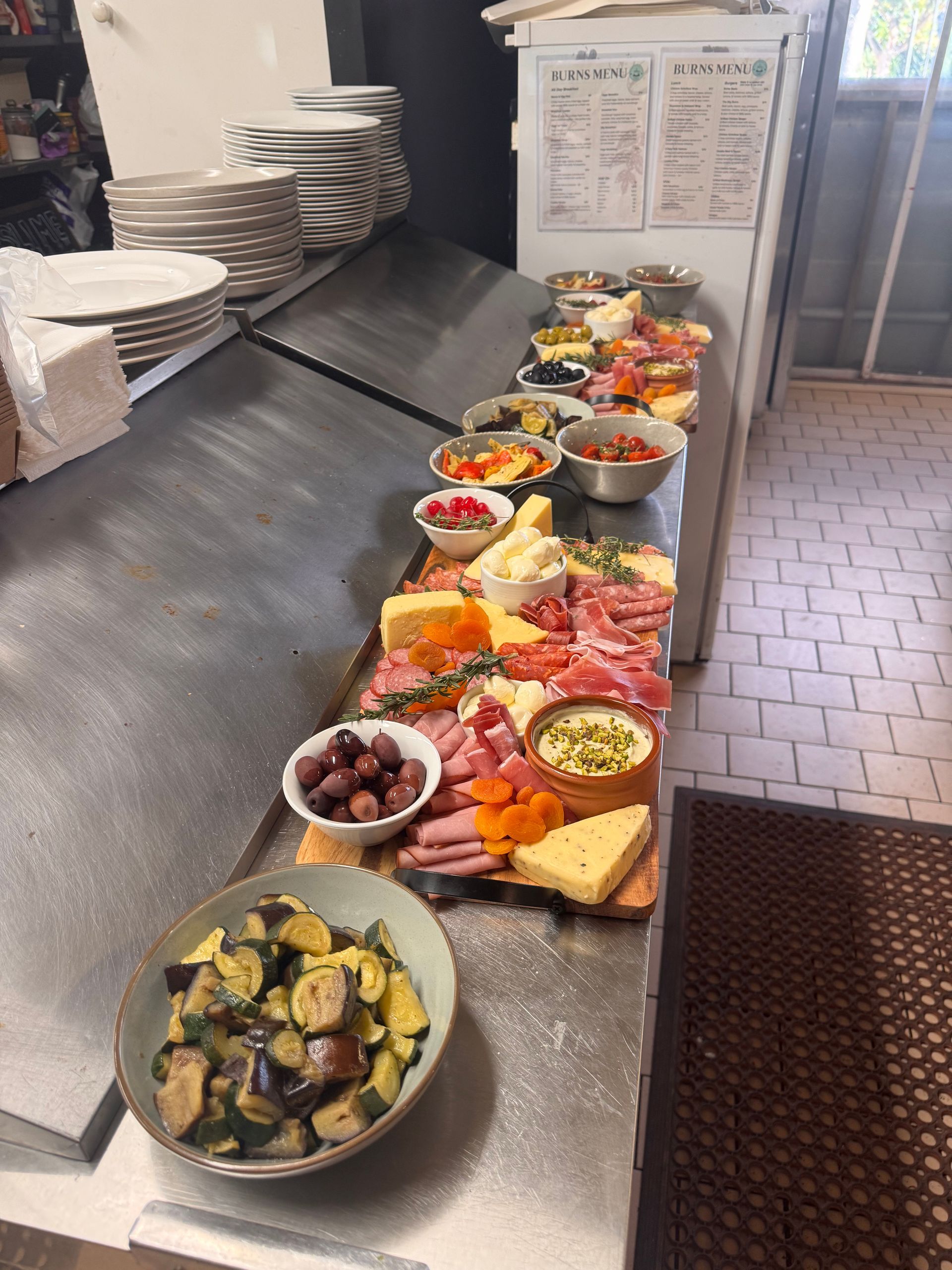 A food prep station in a kitchen features a wooden charcuterie board surrounded by small bowls of vegetables and olives — Rustique on the Coast In Ourimbah, NSW