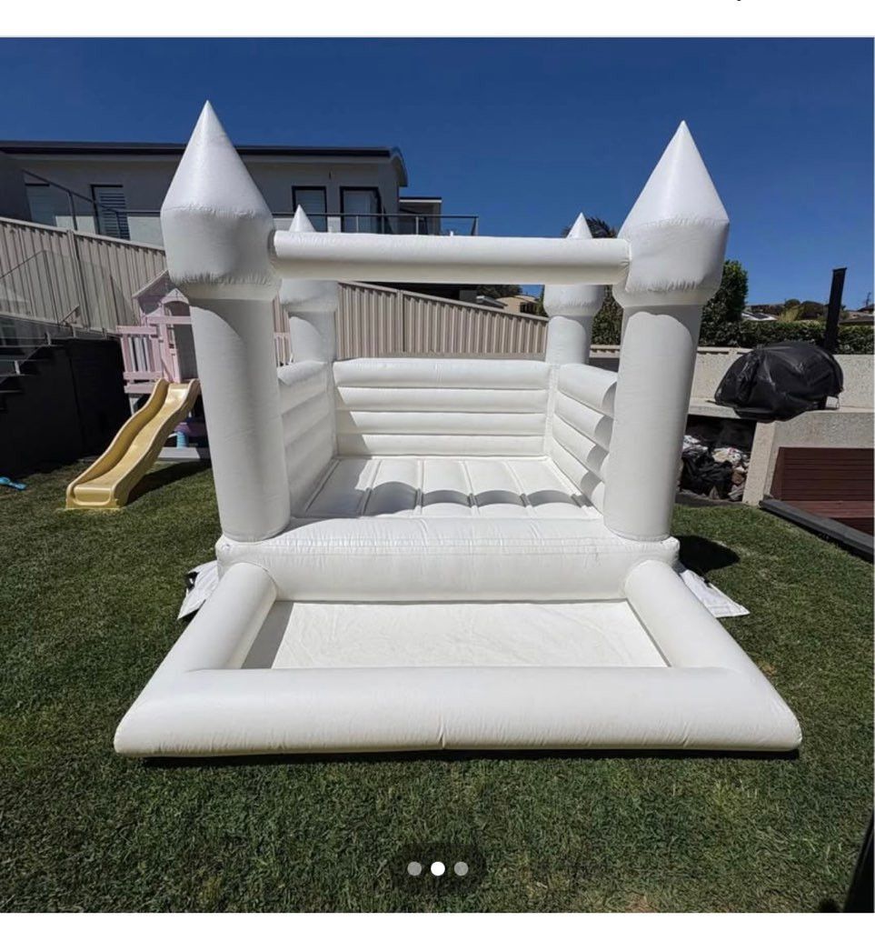 White inflatable bounce house in a backyard, with a slide visible