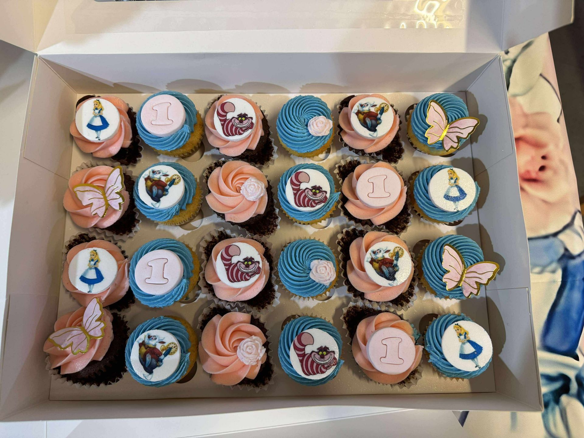 Box of Alice in Wonderland cupcakes: pink, blue frosting, character toppers, and butterflies — Rustique on the Coast In Ourimbah, NSW