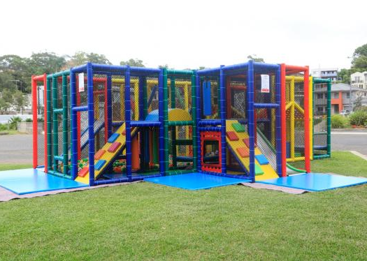 A colorful indoor playground with slides, climbing structures, and blue floor mats on grass.