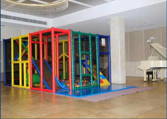 Play structure with slides, tunnels, and ball pit, next to a piano in a brightly lit room.