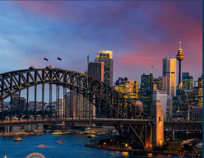 Sydney Harbour Bridge at sunset, cityscape with harbor, skyscrapers, and colorful sky.