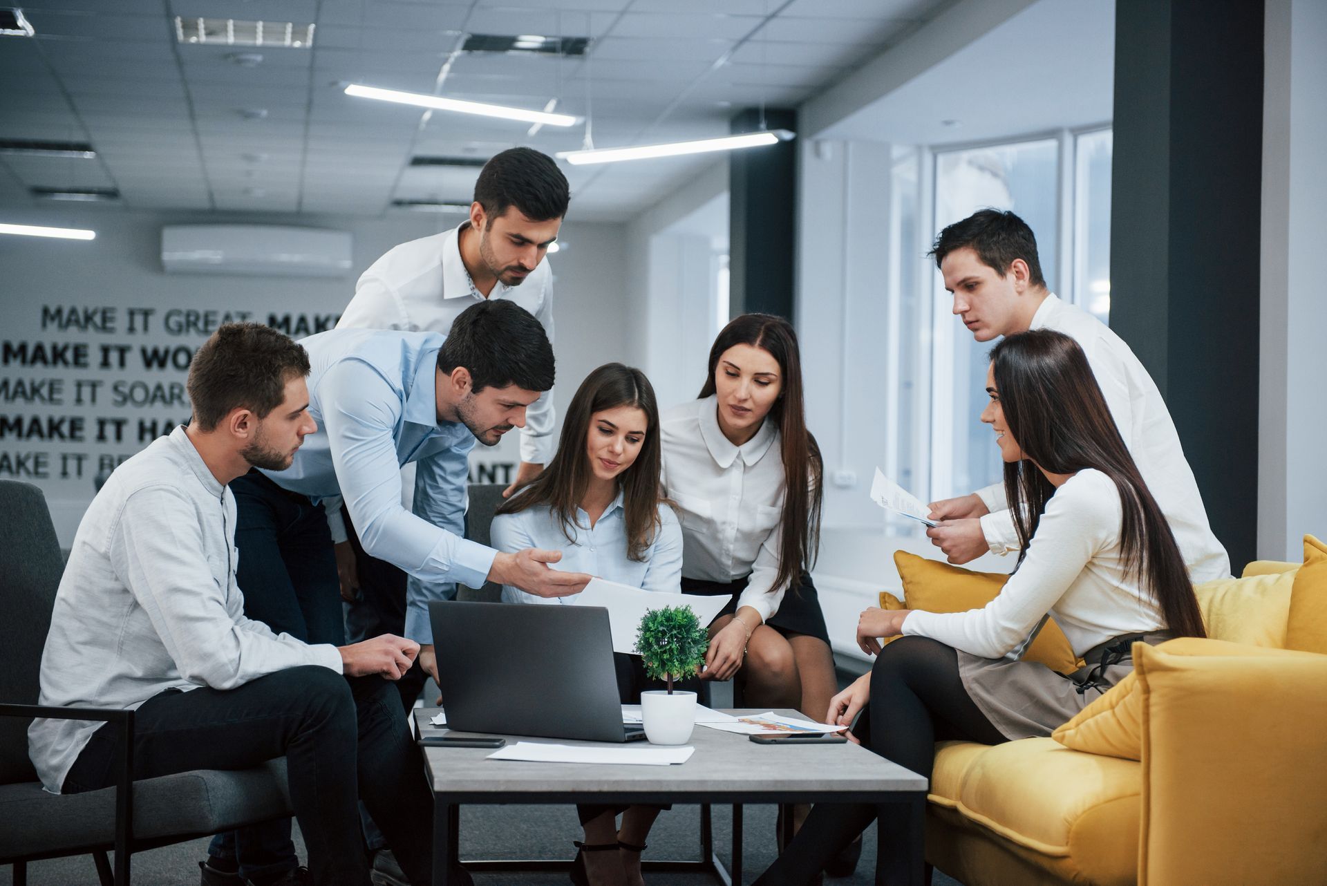 Group of coworkers collaborating around a laptop and papers in a modern office.