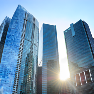 Skyscrapers reaching towards a bright sun, blue glass exteriors.