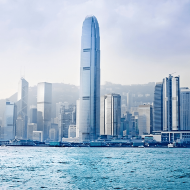Hong Kong skyline with tall skyscrapers, including the International Finance Centre, overlooking the water on a hazy day.