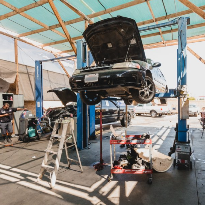 A black car on a lift with its hood open inside a car repair shop, a mechanic nearby. | Universal Brakes & Alignment