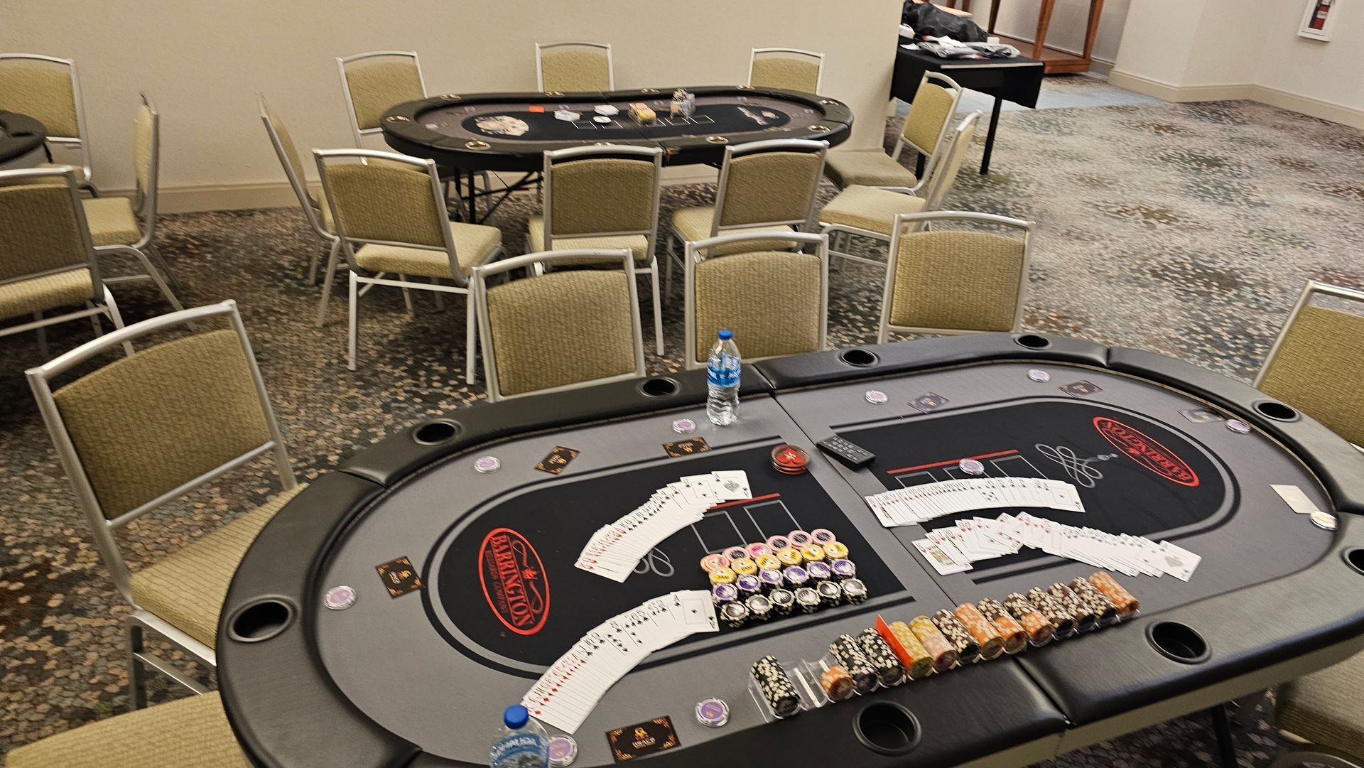 A poker table with cards and chips on it in a room with chairs.