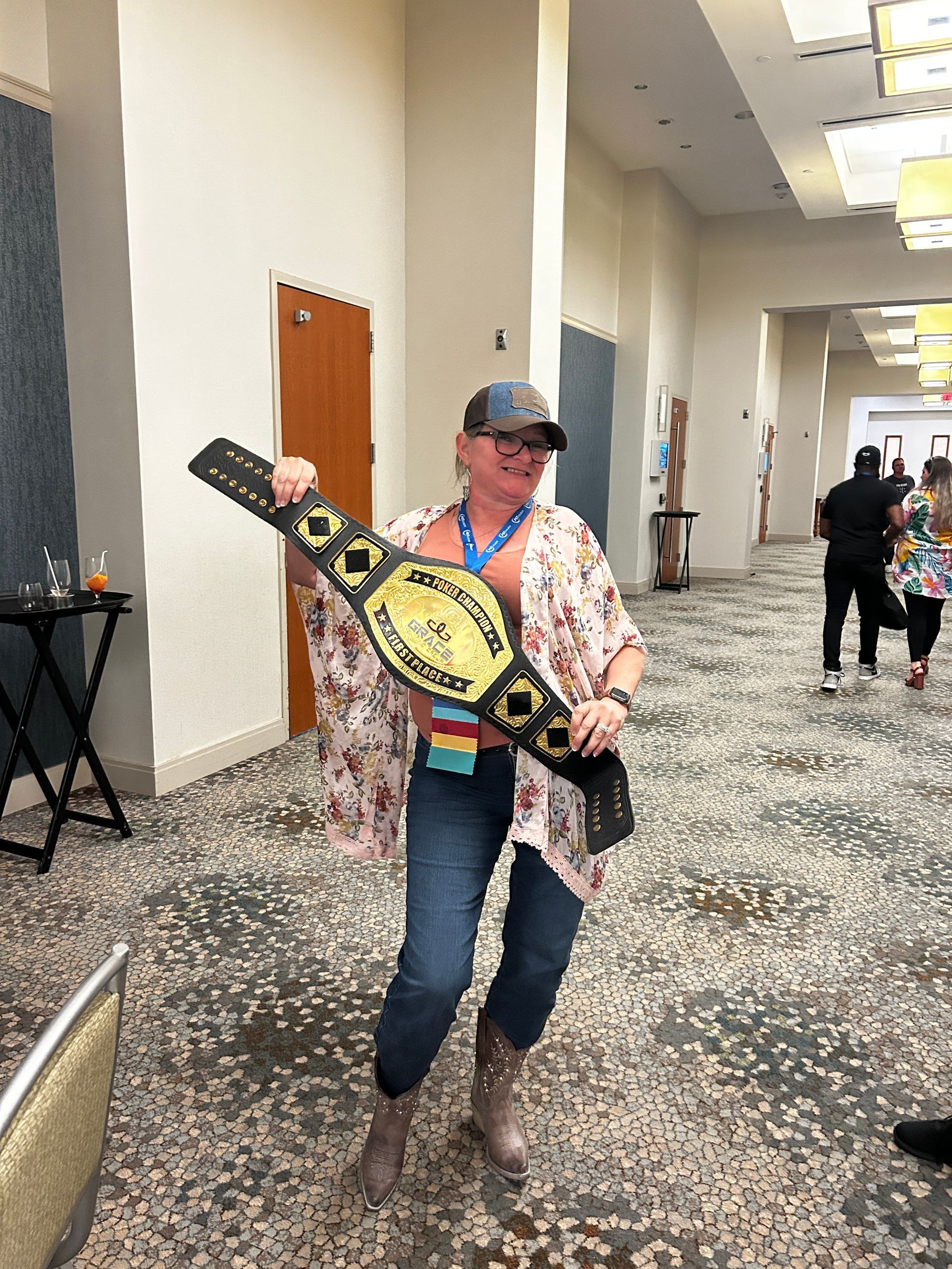 A woman is holding a wrestling belt in a hallway.