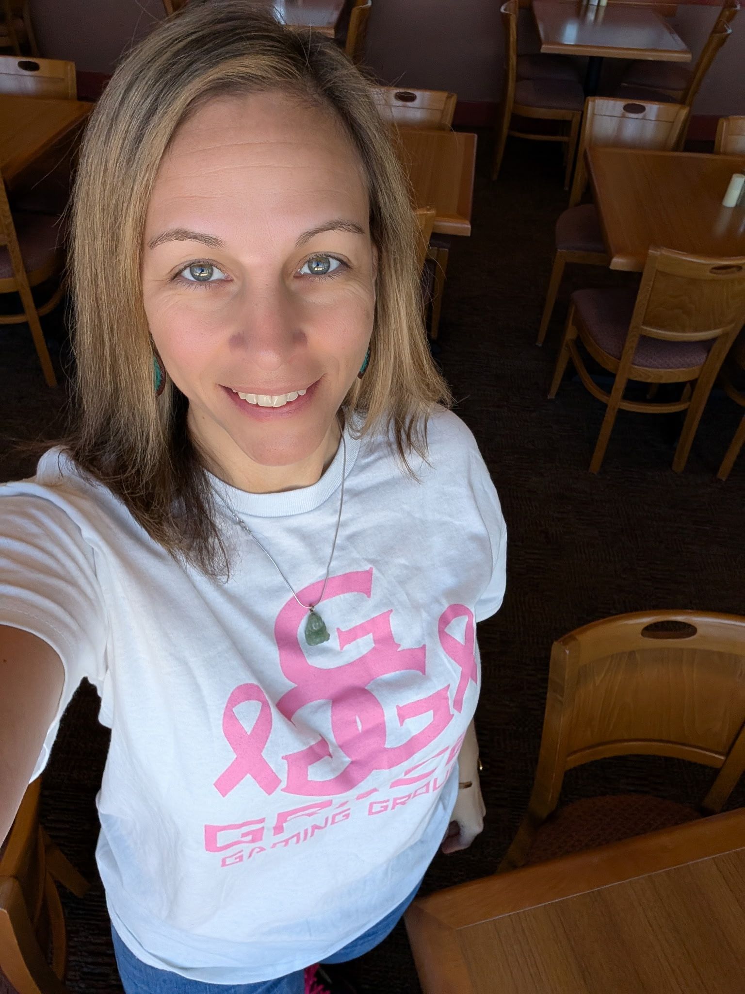A woman wearing a pink ribbon t-shirt is taking a selfie in a restaurant.