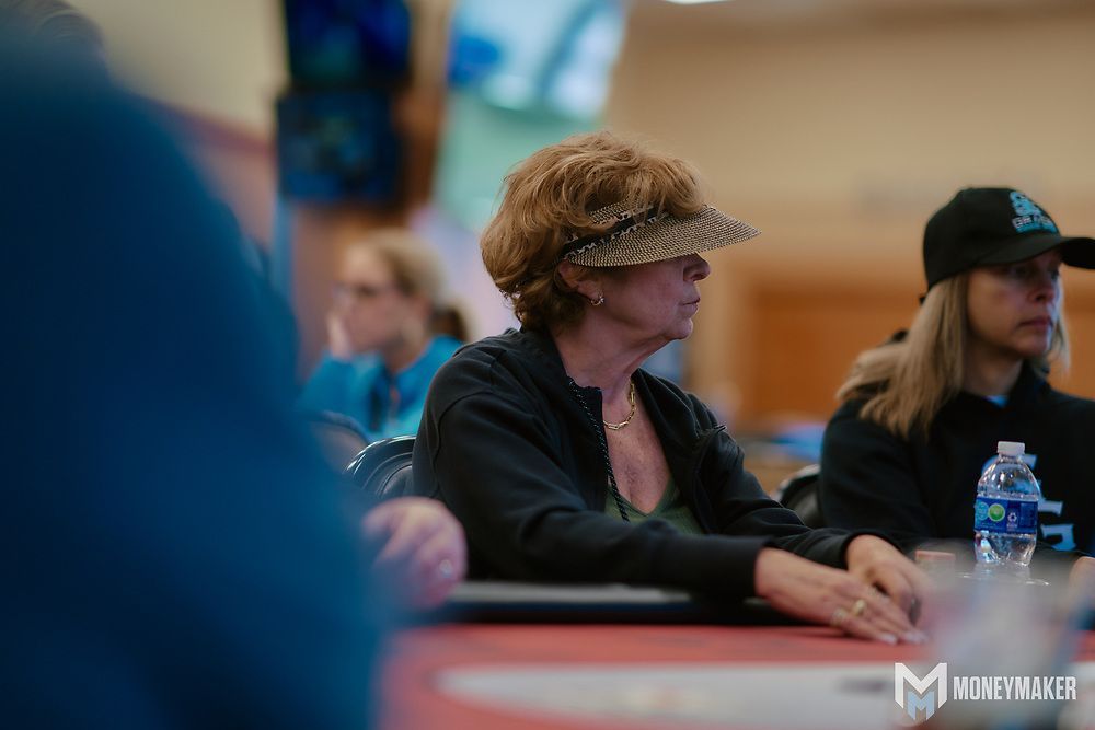 A woman wearing a visor is sitting at a table playing poker.