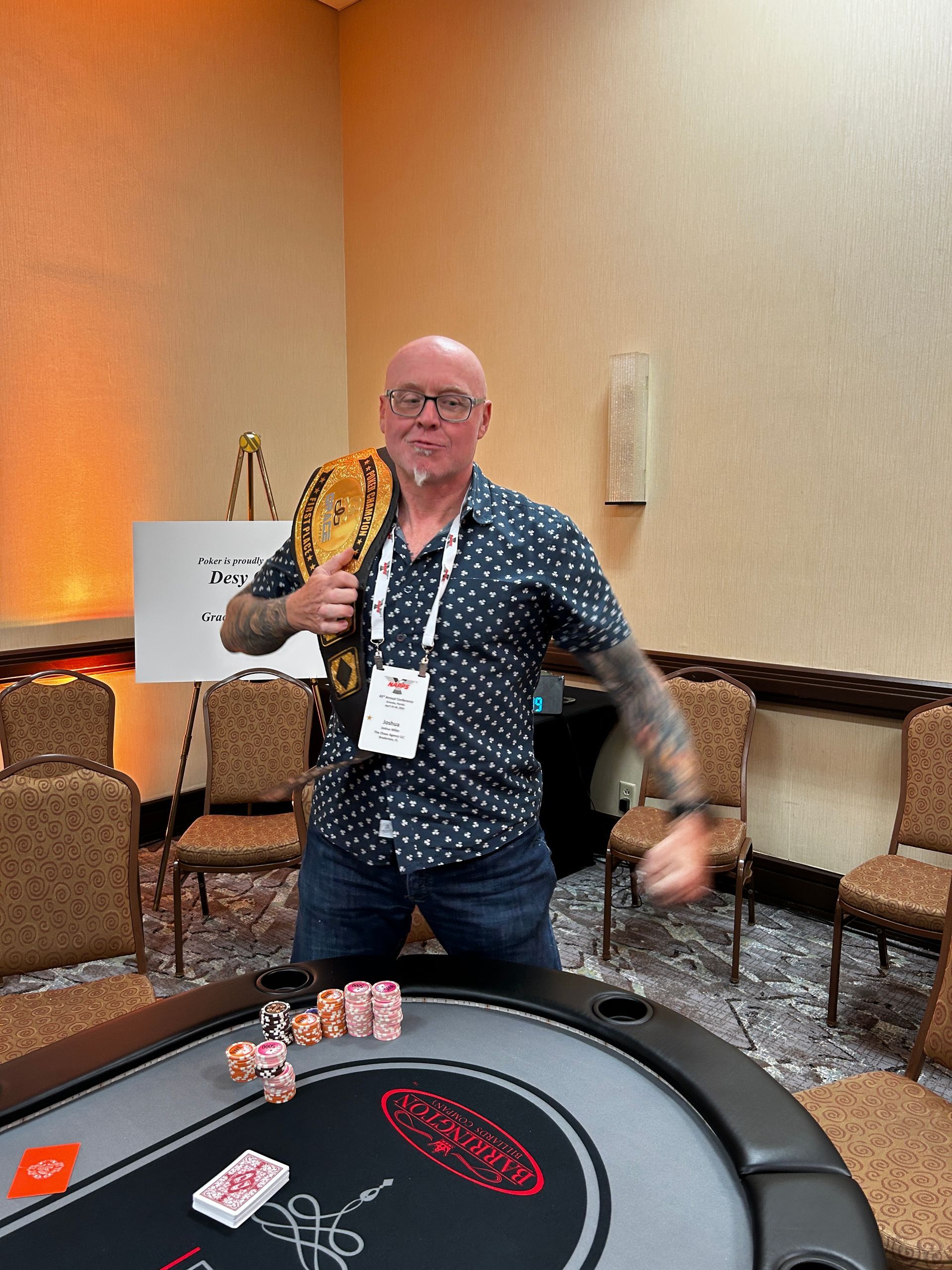 A man is standing in front of a poker table holding a trophy.