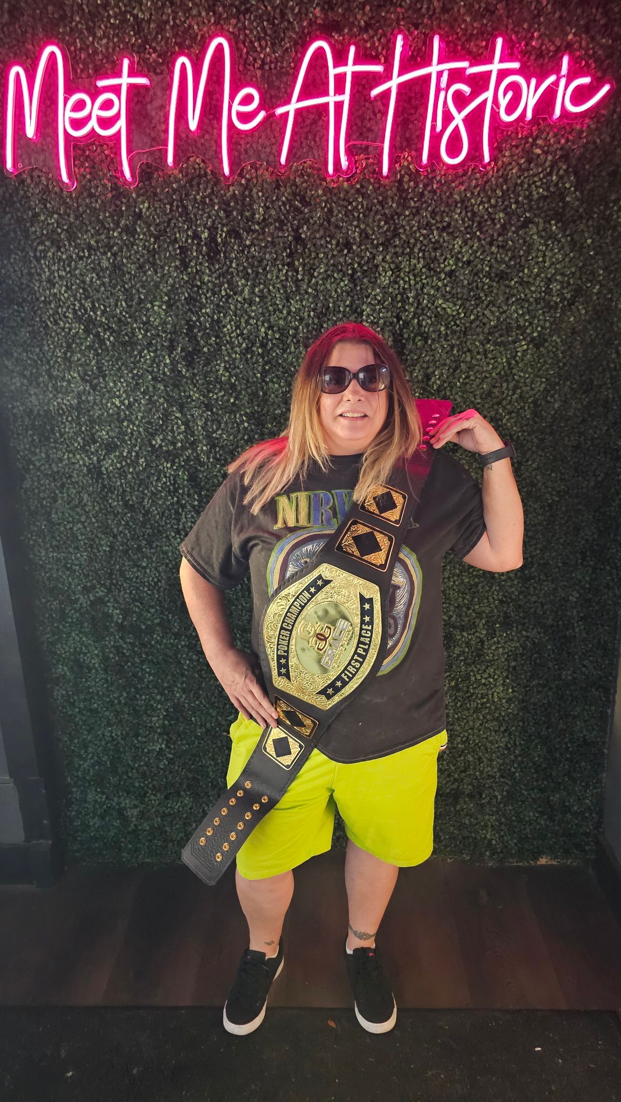 A woman is standing in front of a neon sign that says meet me at historic.