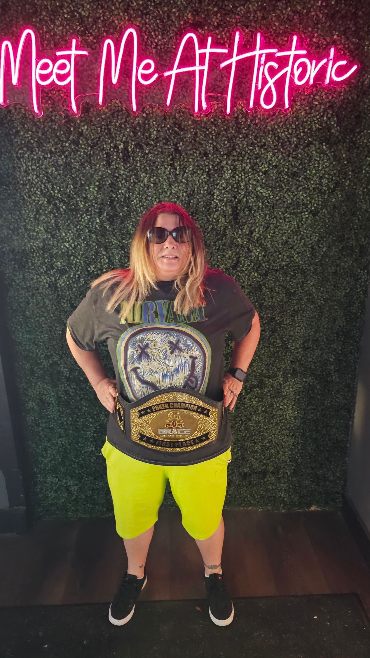 A woman is standing in front of a neon sign that says meet me at historic.