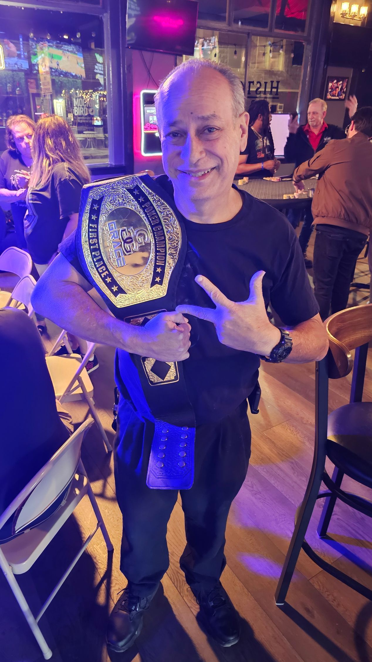 A man is holding a wrestling belt in a bar.