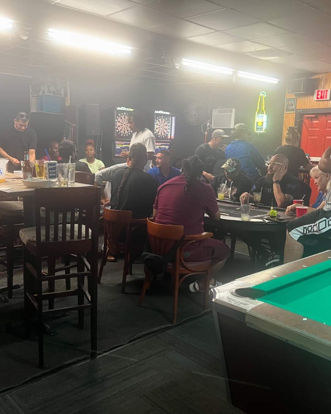 A group of people are sitting at tables in a bar with a pool table.