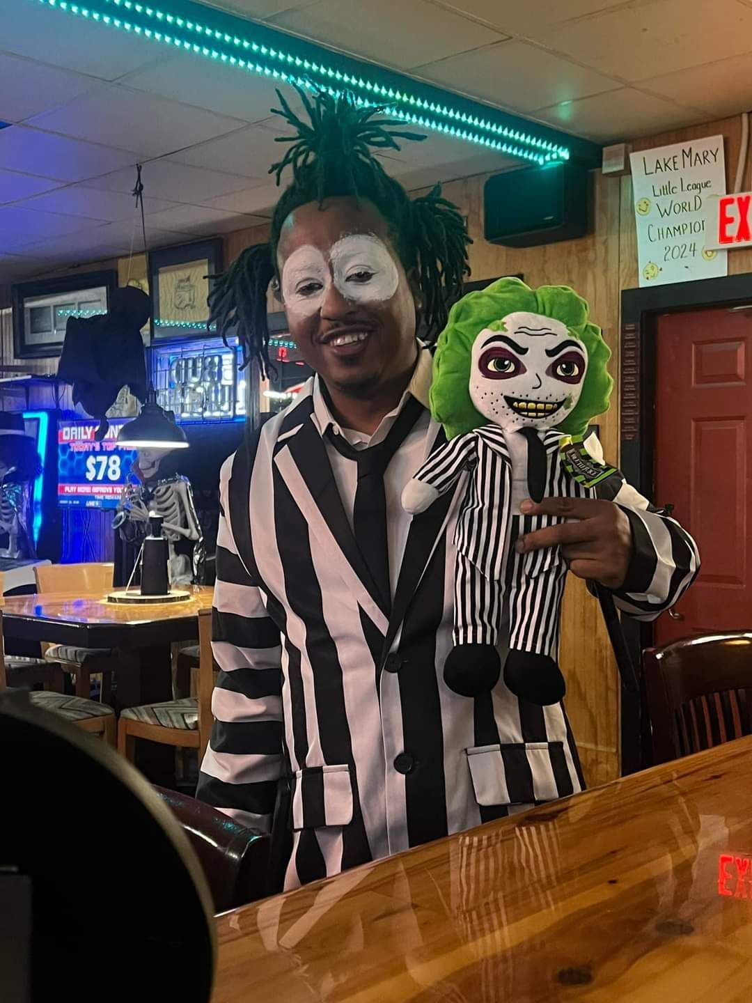 A man in a striped suit is holding a stuffed joker doll.