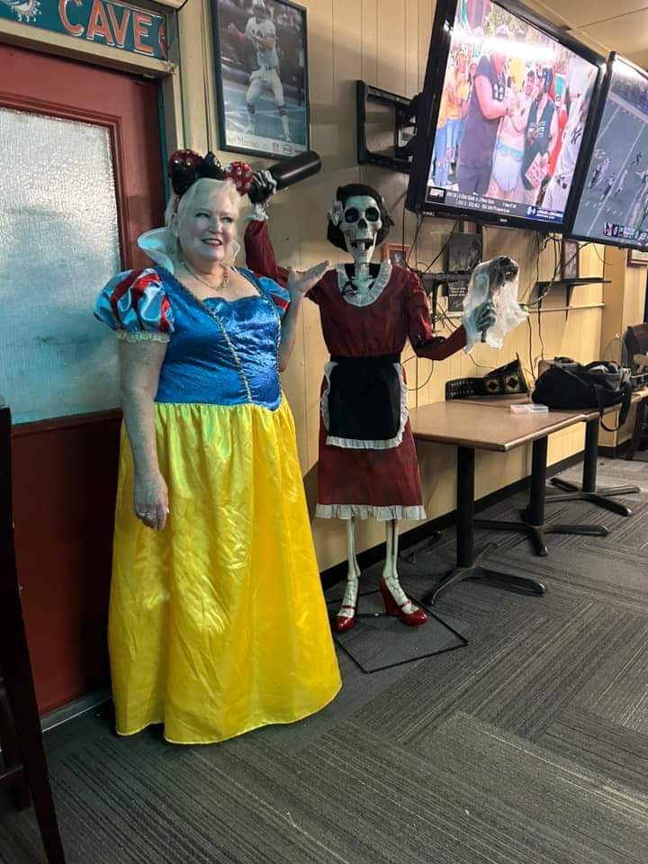 A woman in a snow white costume is standing next to a skeleton.