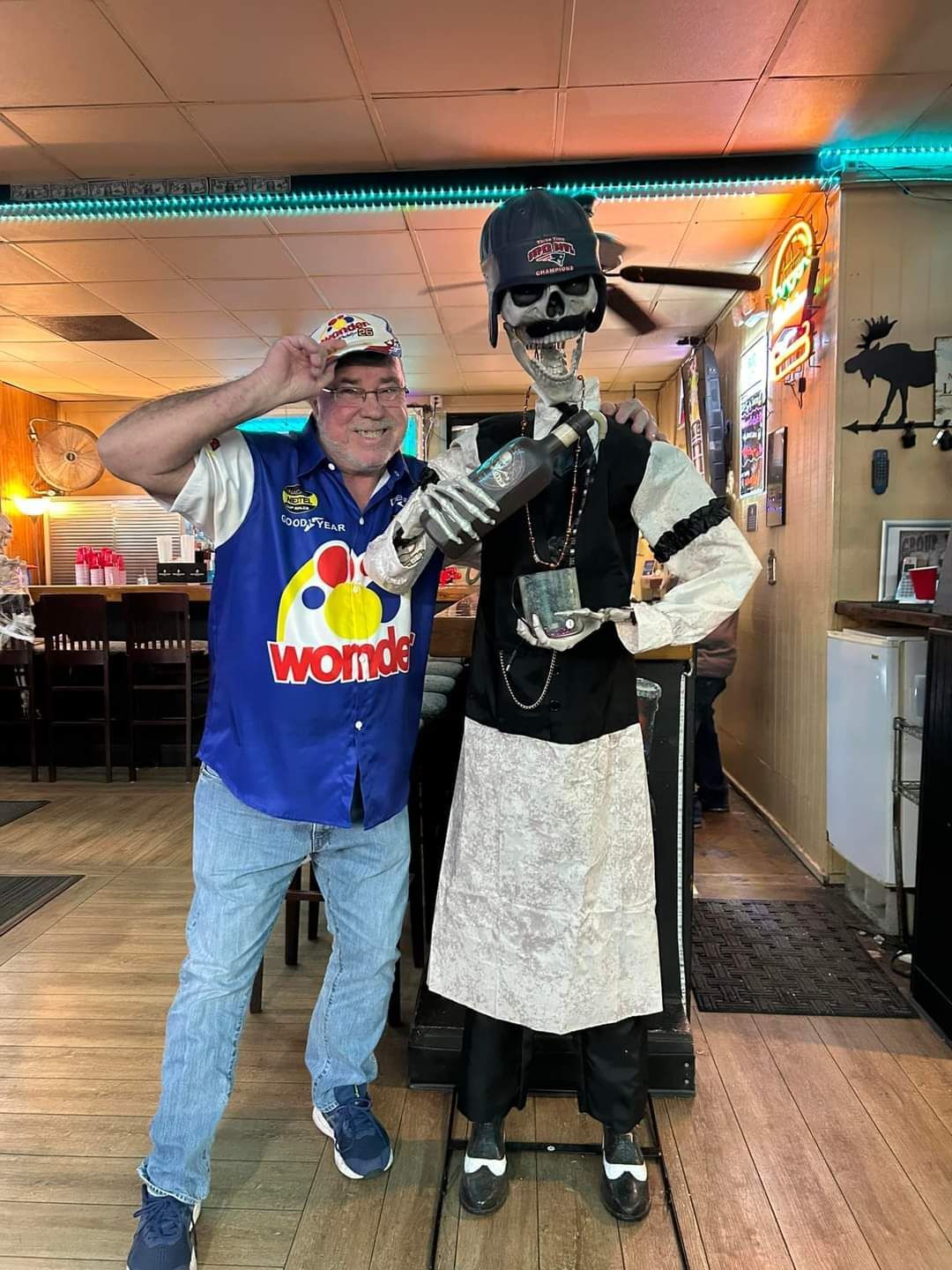 A man is standing next to a skeleton statue in a restaurant.