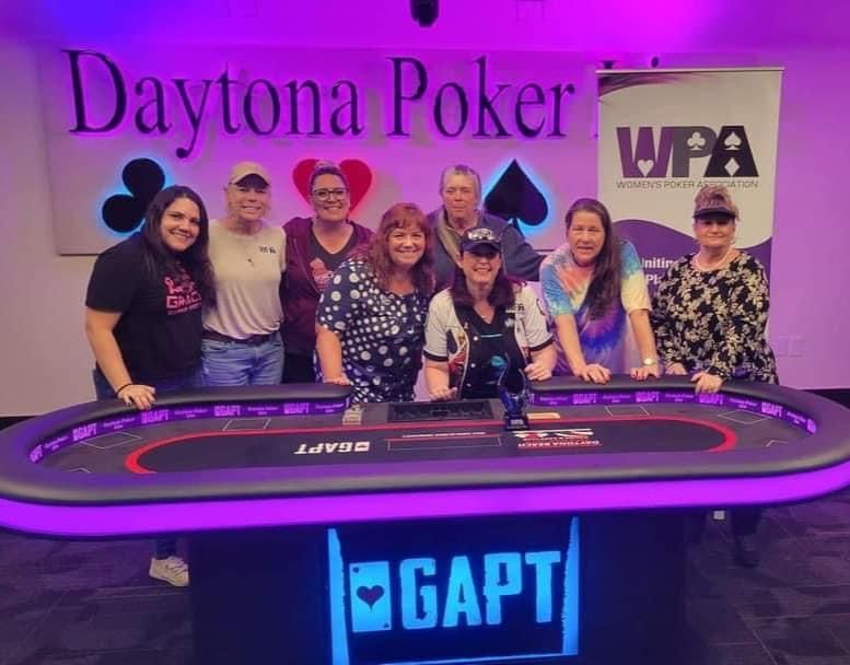 A group of people are posing for a picture in front of a daytona poker table