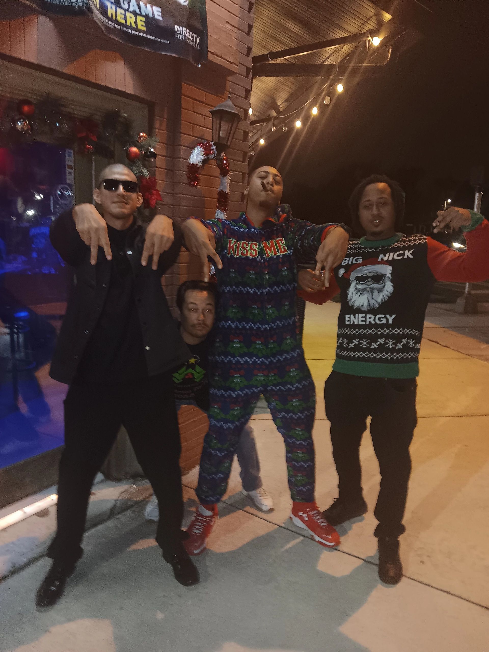 A group of men posing for a picture with one wearing a sweater that says merry christmas