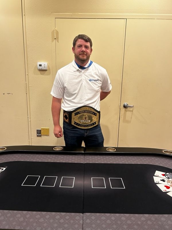 A man wearing a wrestling belt is standing in front of a poker table