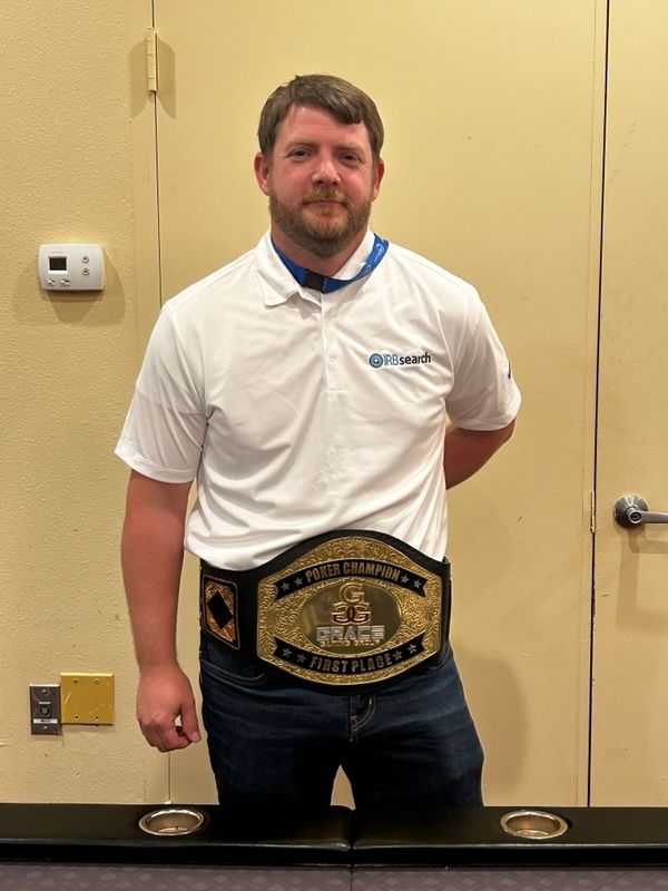 A man wearing a wrestling belt is standing in front of a door.