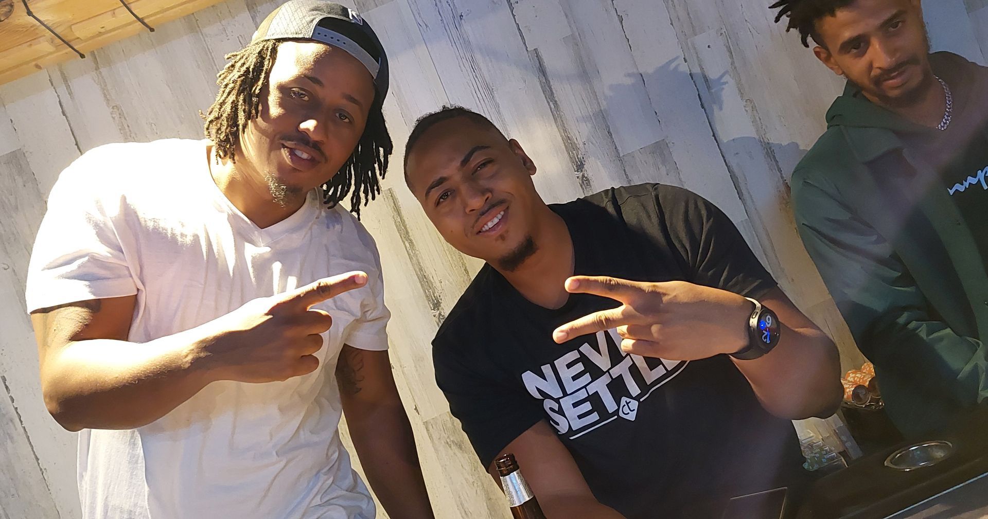 Three men are posing for a picture and one of them is wearing a shirt that says never settle