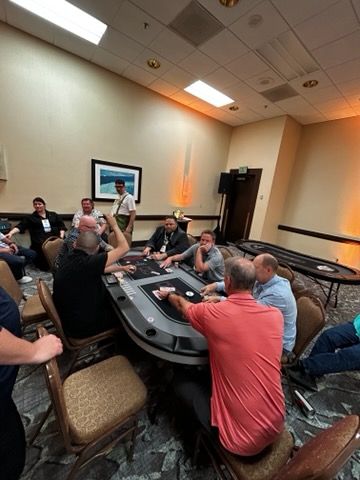 A group of people are sitting around a poker table in a room.