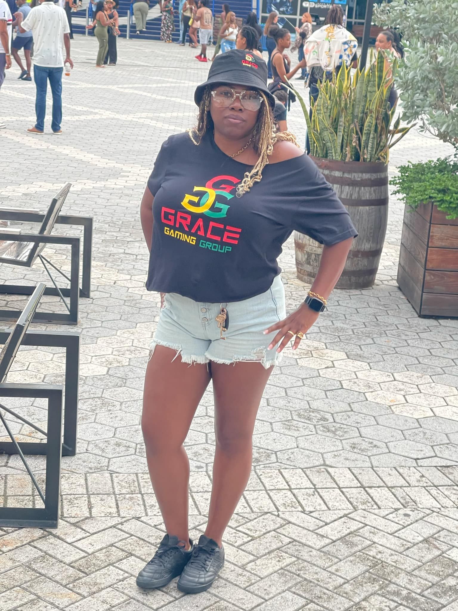 A woman wearing a black t-shirt with the word grace on it is standing on a brick sidewalk.