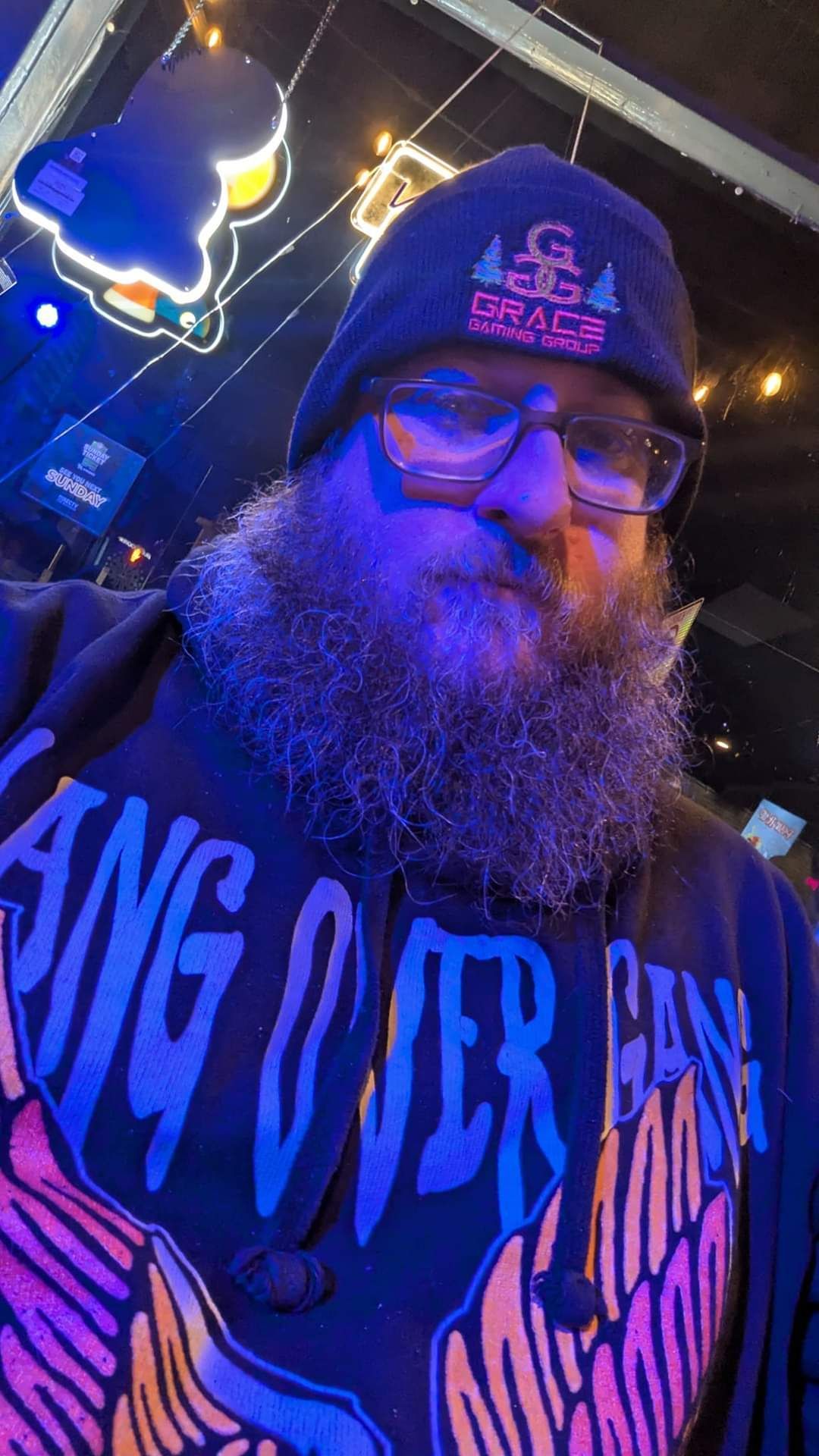 A man with a beard wearing glasses and a beanie is taking a selfie.