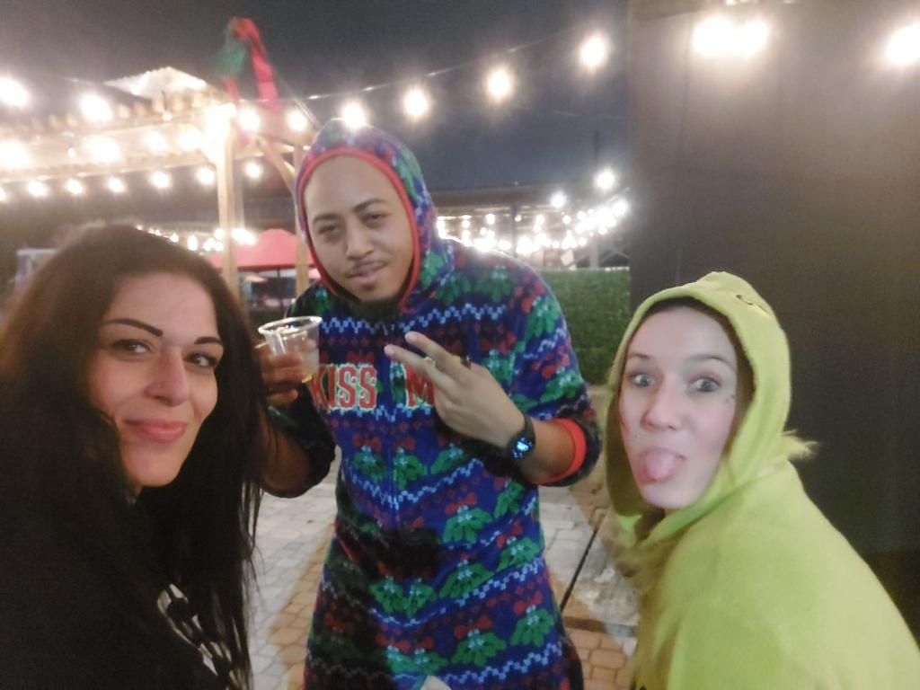 Three people are posing for a picture and one of them is wearing a christmas sweater.