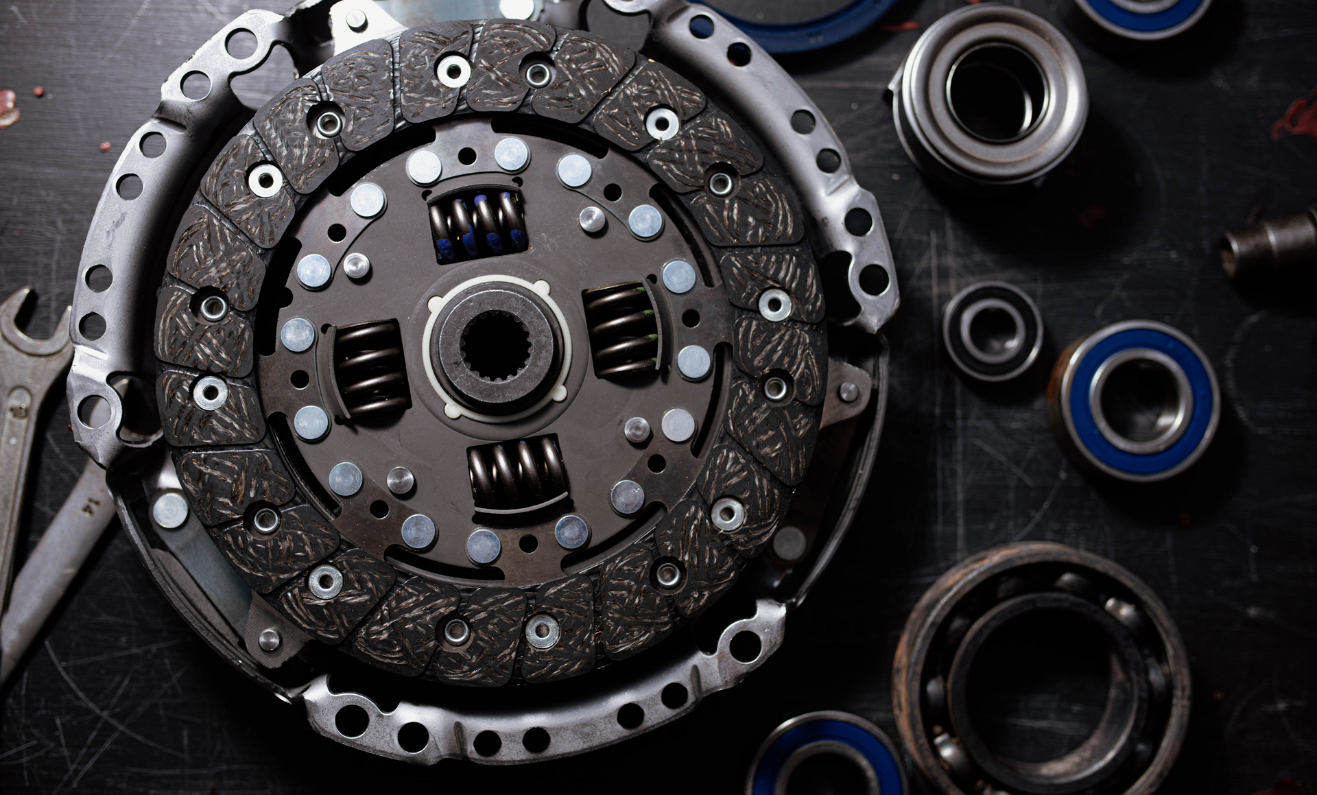 A close up of a clutch disc surrounded by bearings and a wrench.