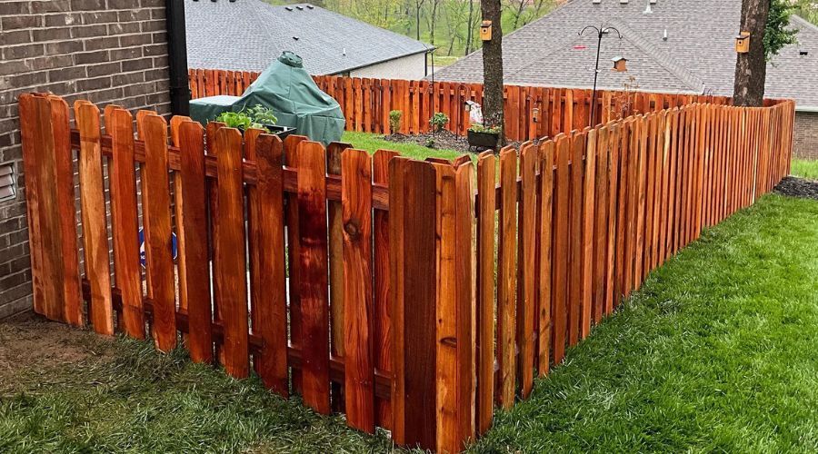 A warm-toned, reddish-brown stained cedar picket fence with dog-ear tops, providing a durable and at